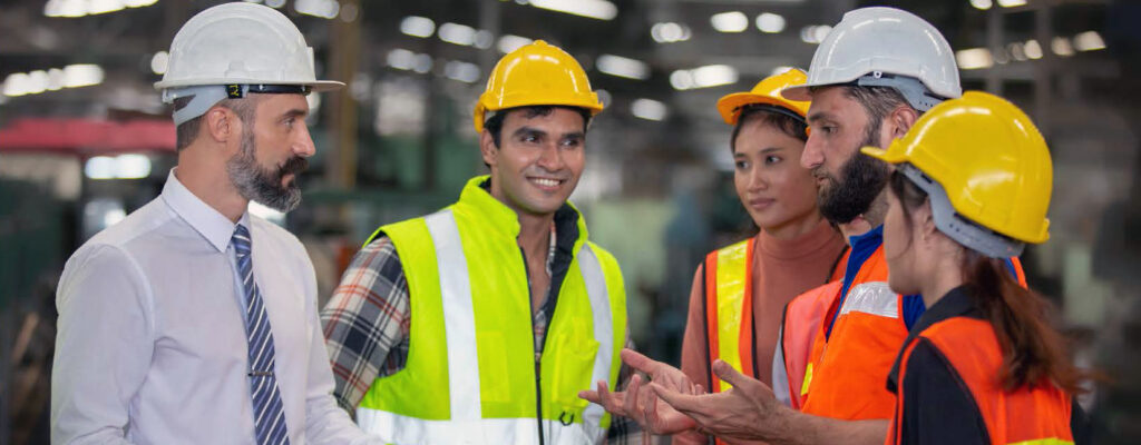 A group of people in hardhats talk on a factory floor.